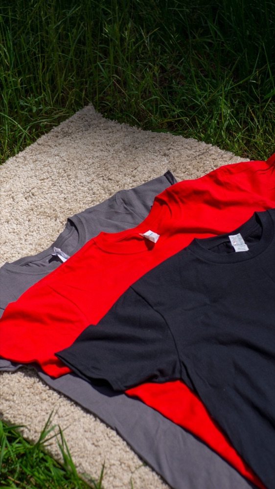 Bedrukte T-shirts in grijs, rood en zwart op een kleed in het gras
