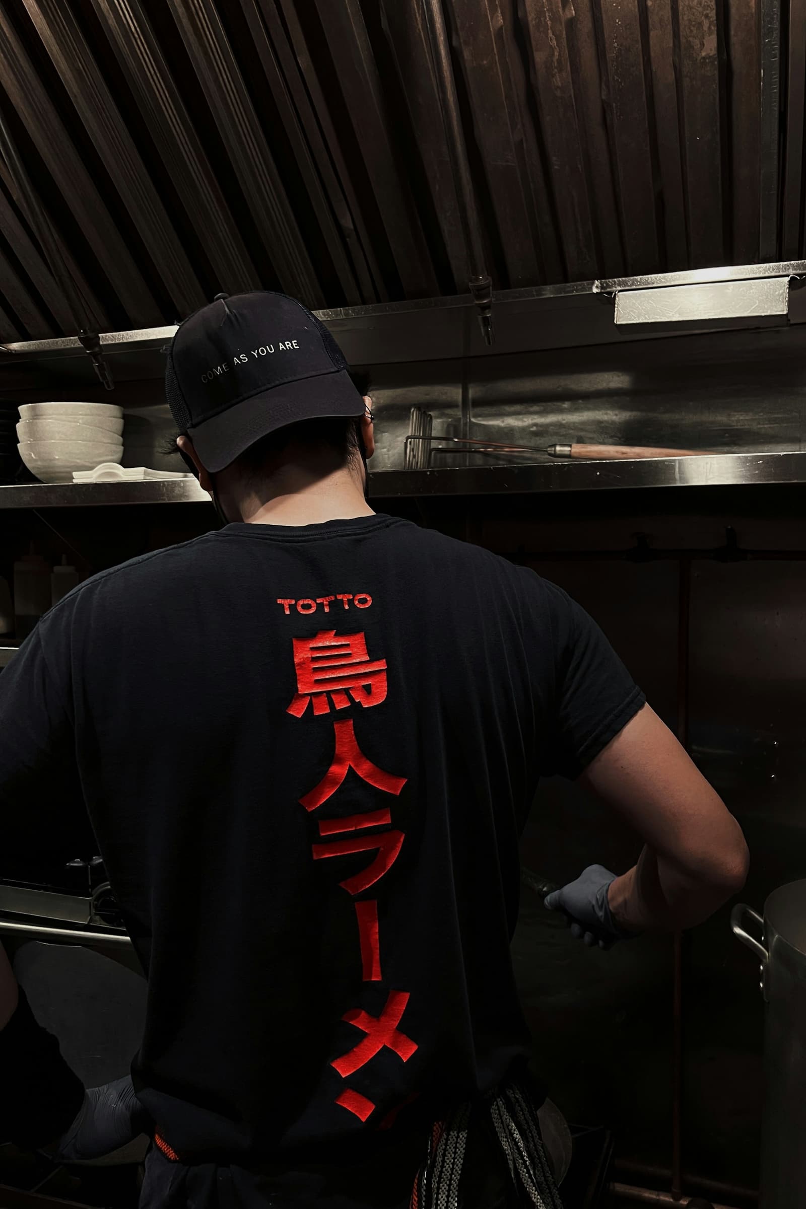 Kok in een zwart shirt met rugprint aan het werk in een horecakeuken